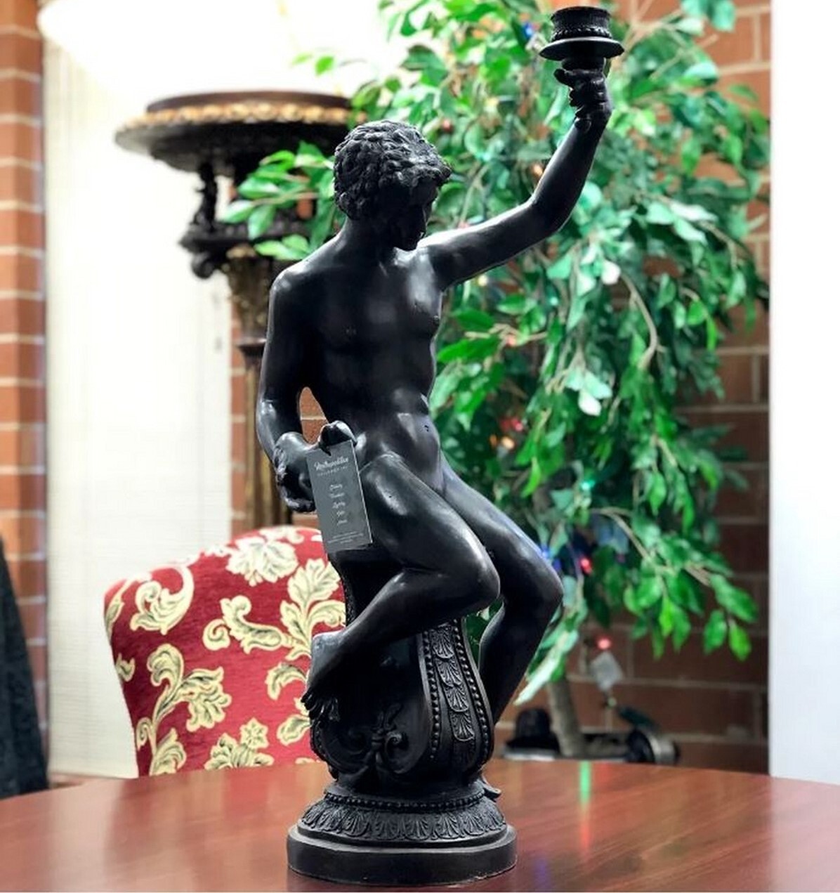 This tabletop sculpture features a bronze man holding a candle holder while sitting atop an ornate bronze base.